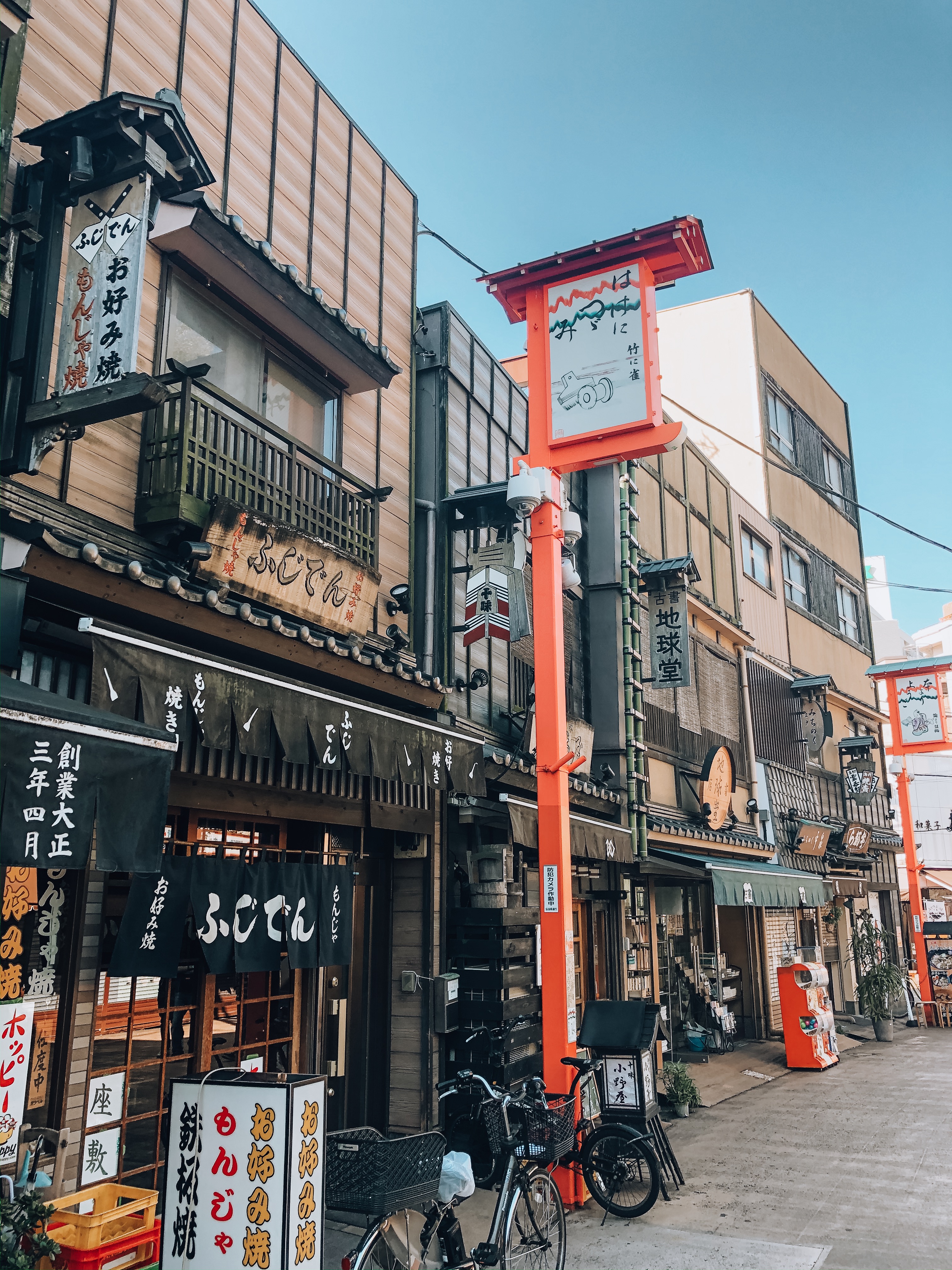 Traditional shopping street in Japan with noren curtains, signage in kanji, and a red torii-style lantern post. Photographed November 2019, iPhone 8. Editorial license via Scopio (ID: 40a3a368-9581-4ae4-839c-14fb0d4253f4).